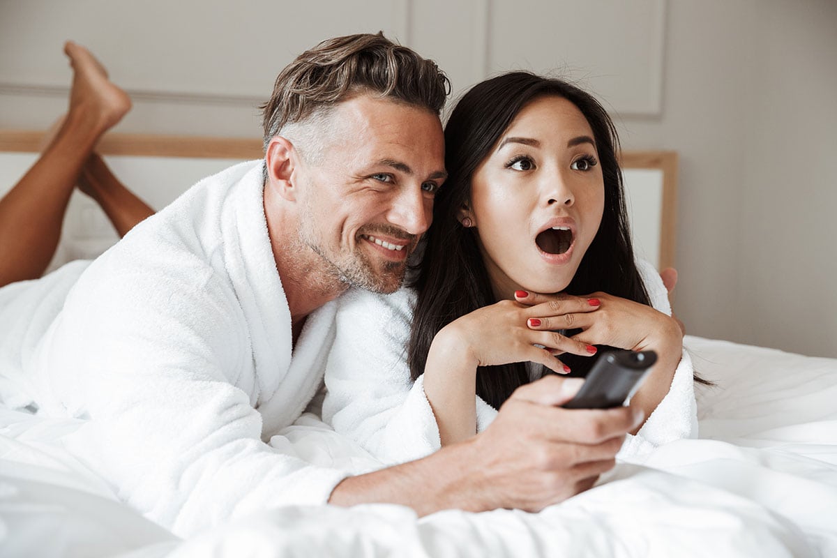 Multi-ethnic couple watching TV in bed. Can CBD help with your libido and sex life?