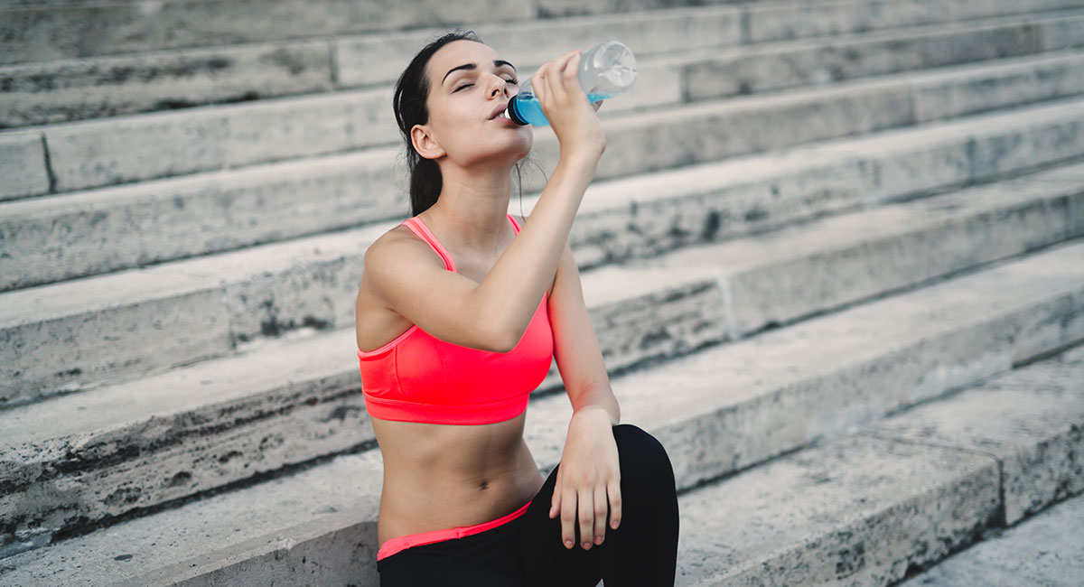 Adult woman drinking water while recovering after a workout. CBD for workout recovery. CBD oil for muscle recovery. Buy CBD for pain online.