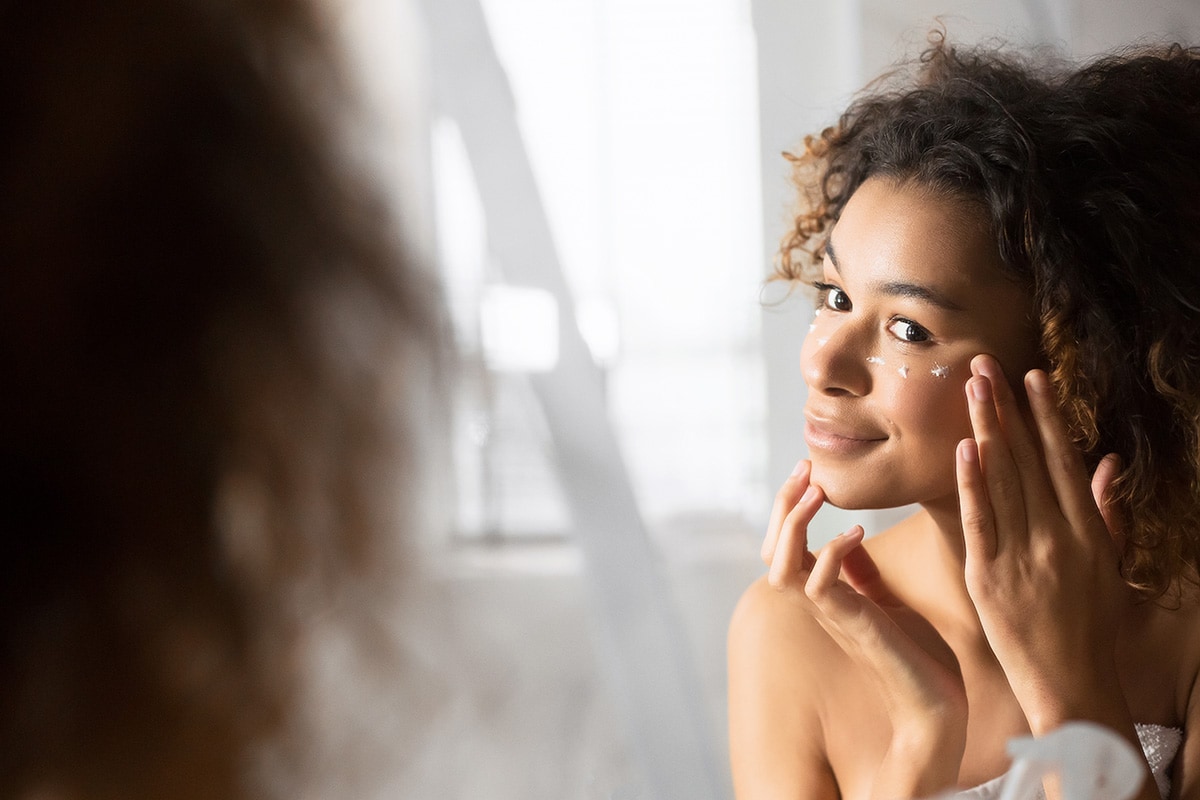 Happy afro girl applying cbd topicals for wrinkles on her face. Buy CBD beauty products and cosmetics online USA.