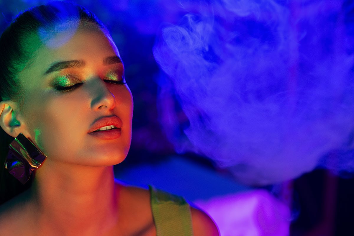 young woman smoking vape in neon blue light. how to use cbd oil for anxiety.